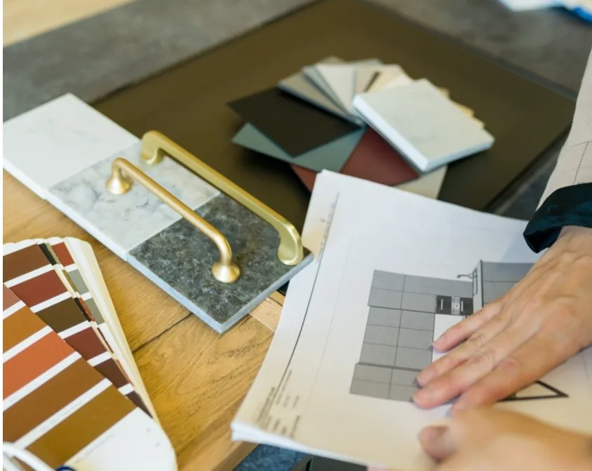 Interior designer reviewing kitchen blueprints next to tile, paint, and cabinet hardware samples.